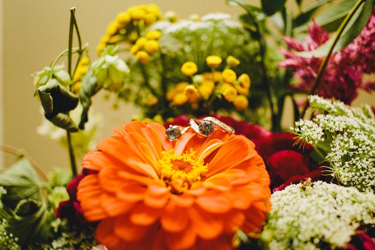Kaleen and Rolly Wedding Rings sitting and bridal bouquet. flowers of orange white and yellow