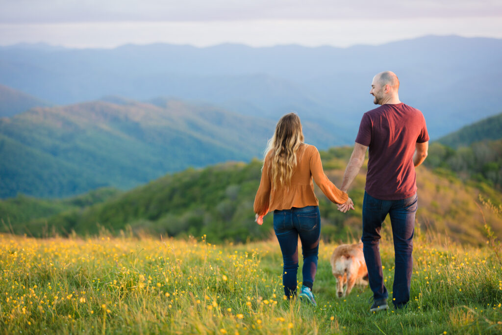 Couple holding hand walking down Appalachian Trail on Max Patch with their dog.