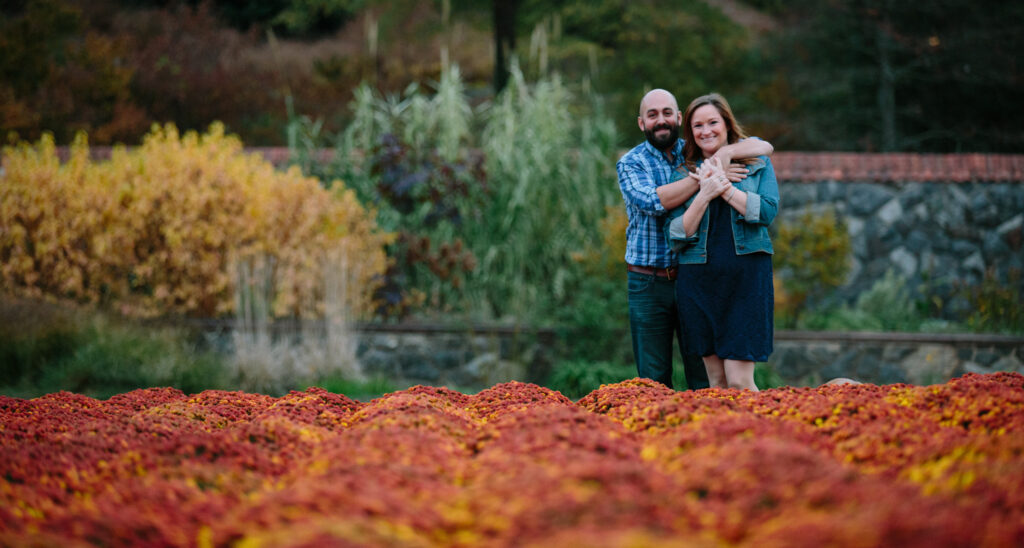 Engagement photo of Eileen and Eser standing in bright red and orange mums in the gardens on Biltmore