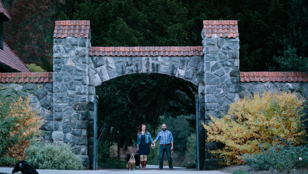Eileen, Eser, and their dog standing in large old stone entrance way into the gardens on Biltmore