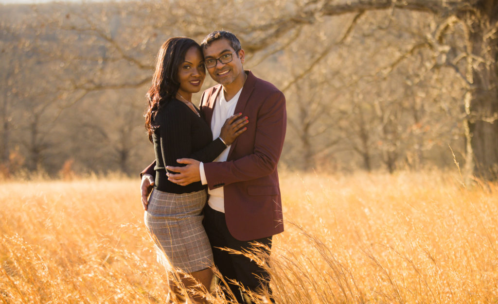 A couple holding one another standing in the fields behind Biltmore Estate. The fields are gold and red creating a very Dynamic engagement photos.