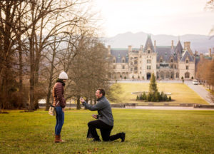 Sam down one one knee proposing to his bride to be with the Biltmore House in the background.