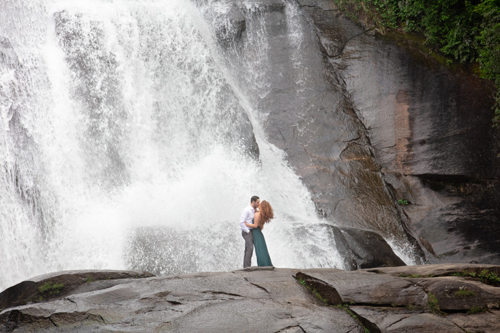 Couple standing at the base of a huge waterfall for the adventure engagement photo session