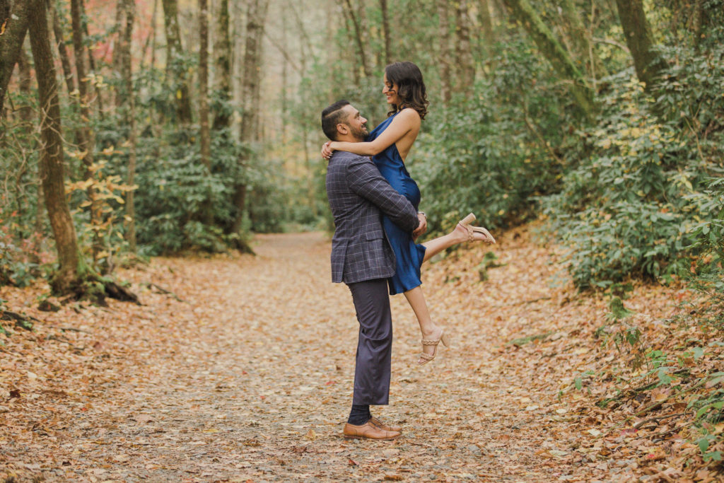 This is one of my favorite photos from the photoshoot. He is picking her up in the air holding her above him, and she is looking down towards him. They are on a beautiful hiking trail in DuPont State Forest with excellent leading lines and unique engagement photos.