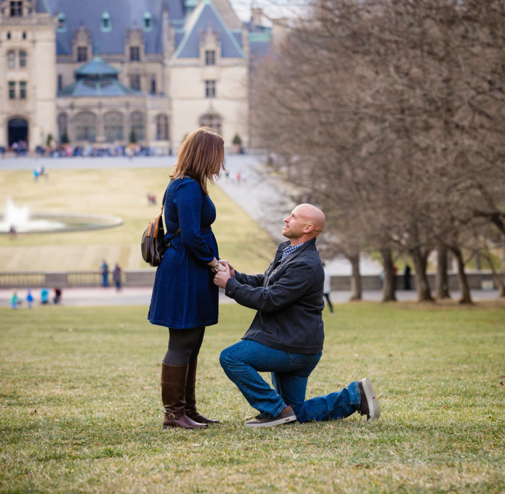 Eric down on one knee at the Biltmore Estate in Asheville, he is proposing to Brittany and the Biltmore House is in the background