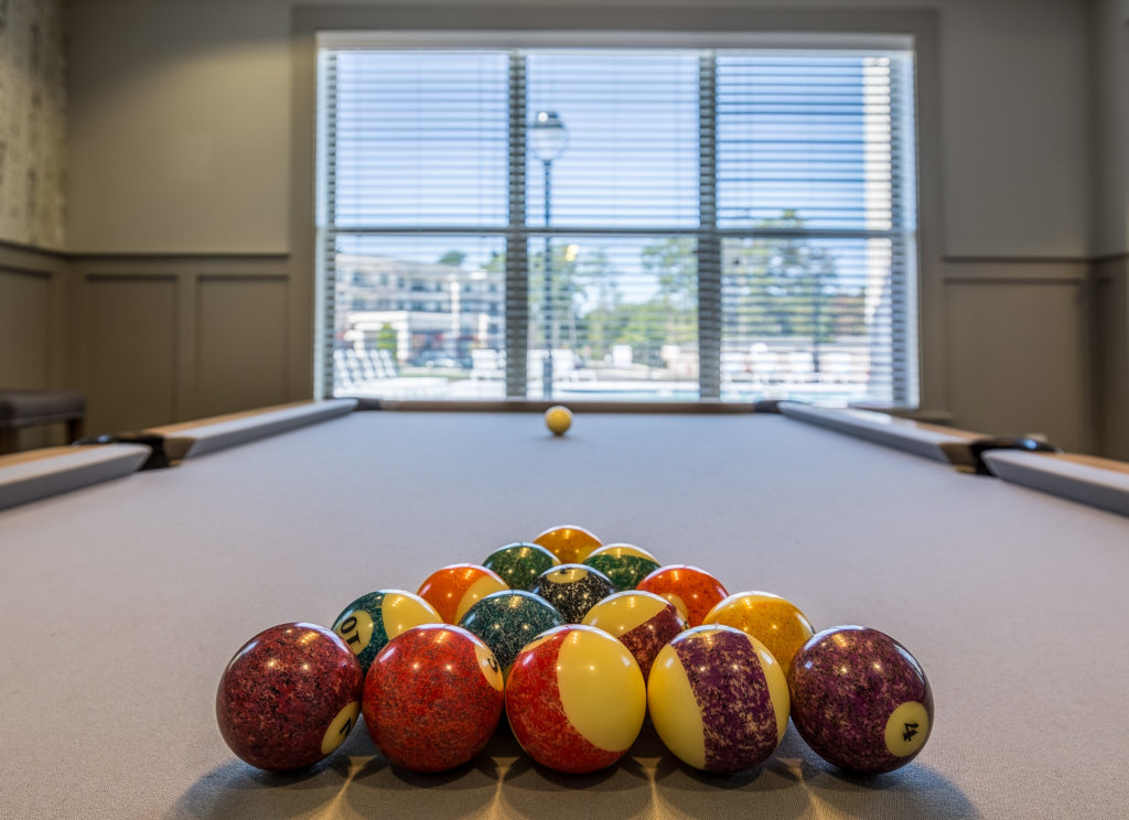 Raleigh Real Estate Photographer took a photo from in the game room at the The Franklin at Crossroads Apartments looking at a full pool table with all the balls racked up ready to play a game.
