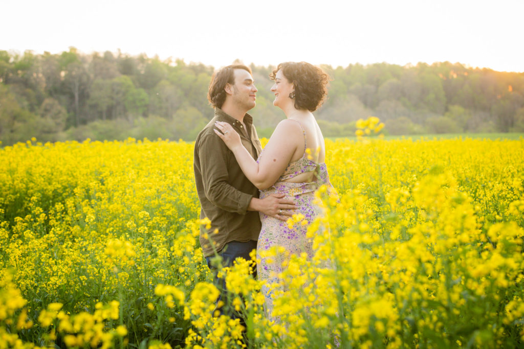 Chloe and Connor standing in a field of yellow flowers, embracing during their engagement photo shoot.