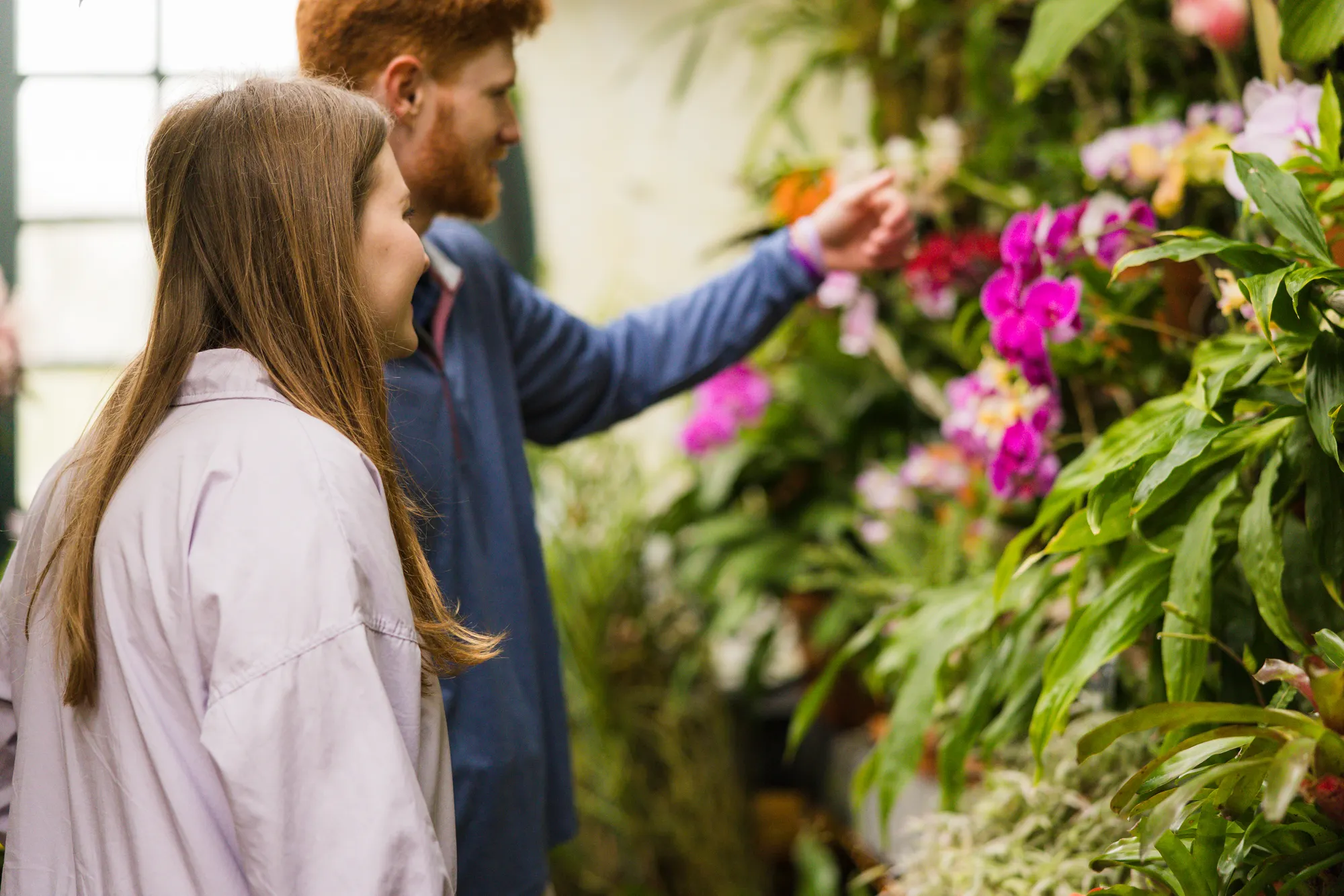 Bride-to-be admiring orchids in the Orchid Room of the Biltmore Conservatory, her fiance blurred in the background
