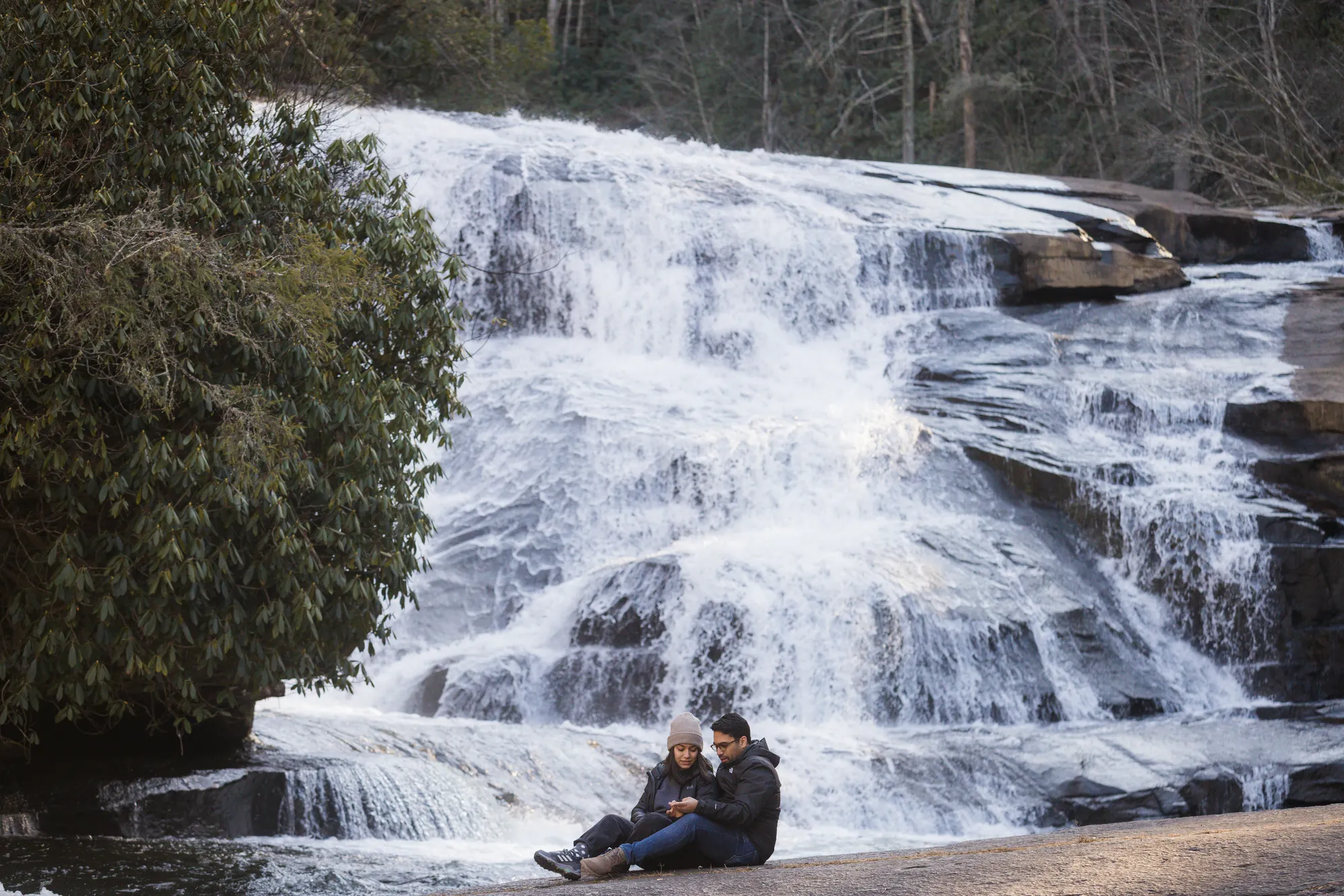 Couple sitting at the base of Triple Falls in winter, DuPont State Forest