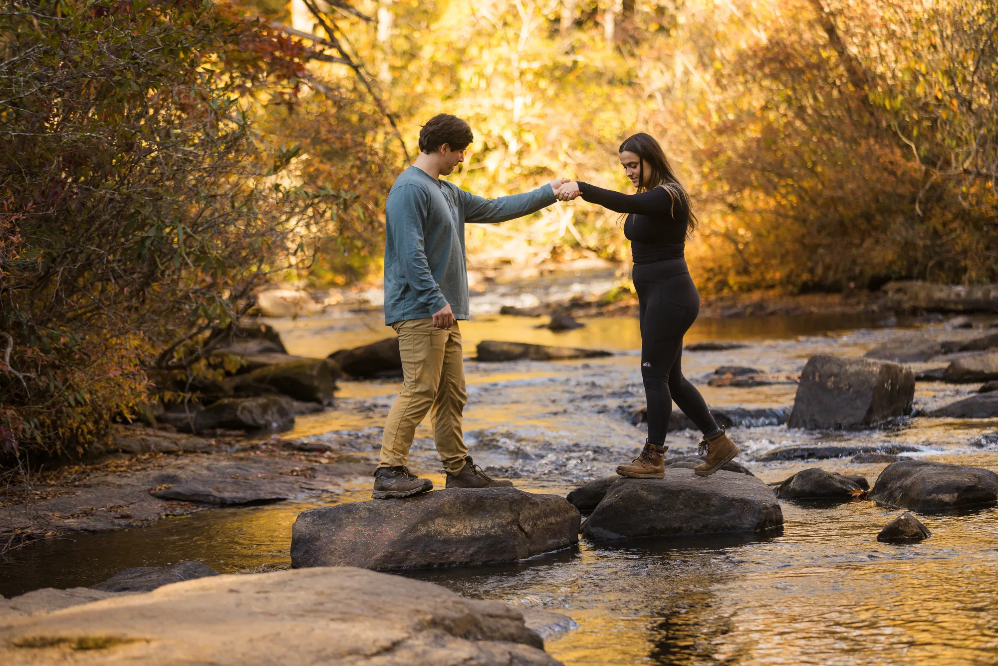 Couple crossing river rocks hand in hand in trail shoes, DuPont State Forest