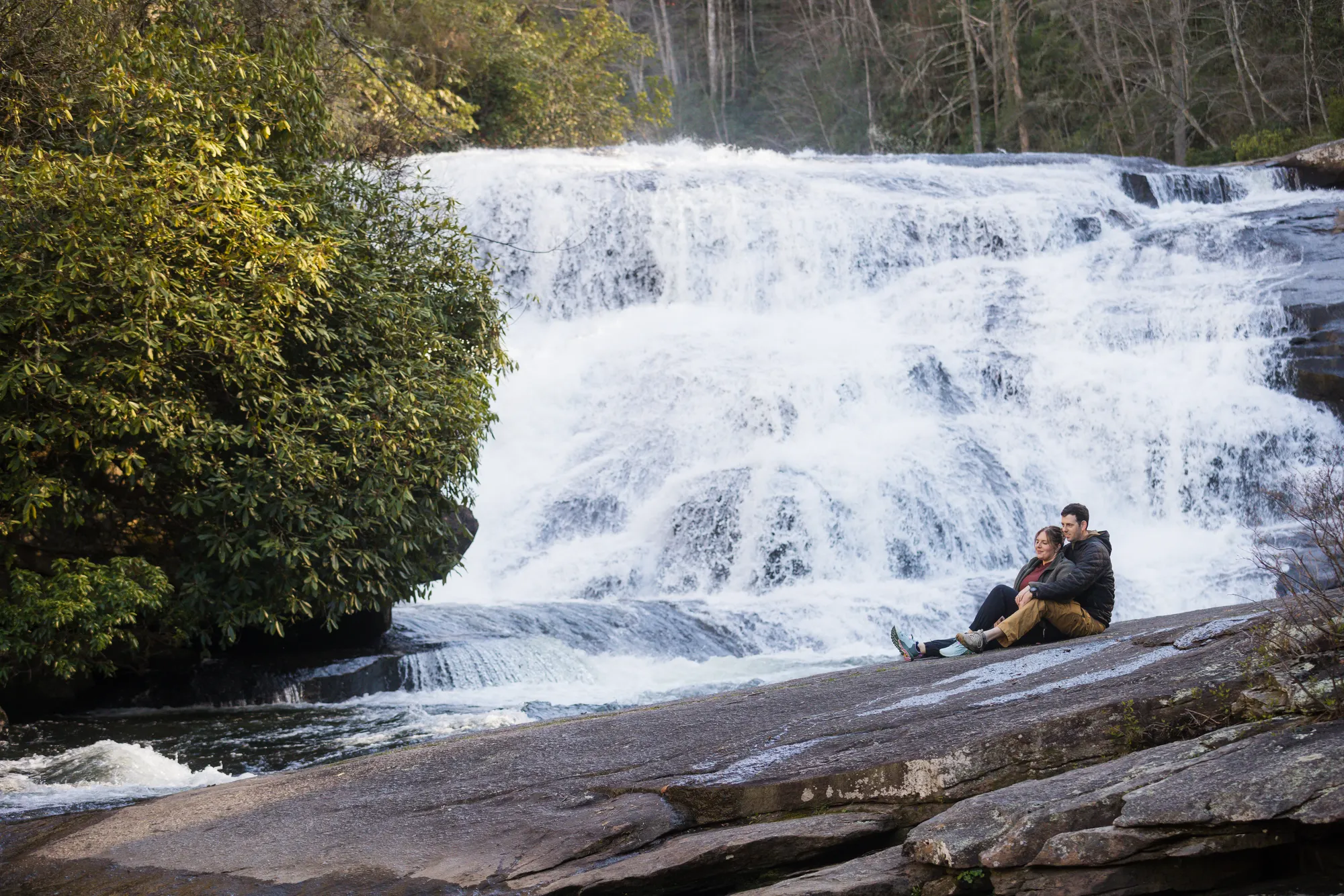 Couple sitting together at the base of Triple Falls, DuPont State Forest