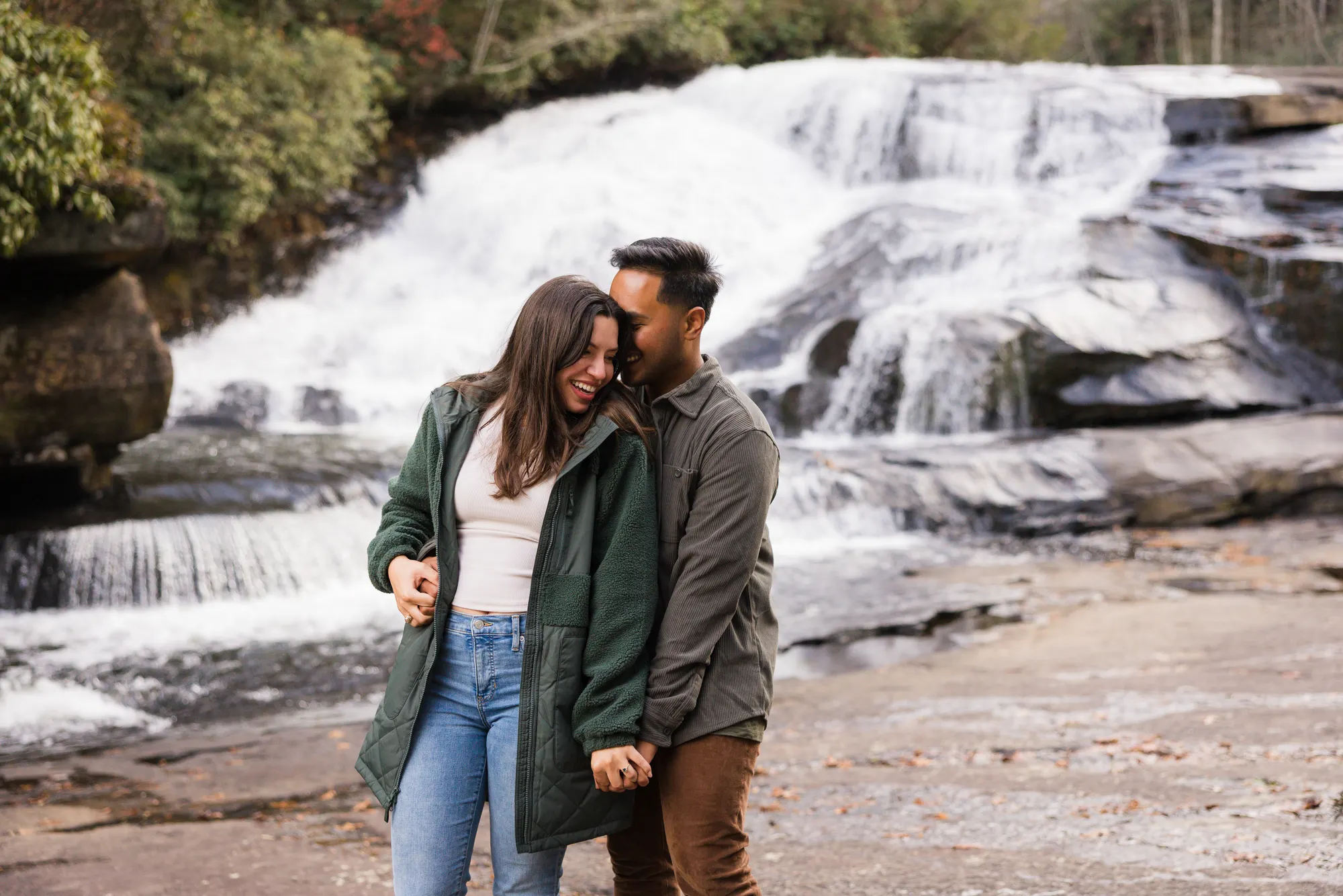 Couple embracing at Triple Falls lower cascade in autumn, DuPont State Forest