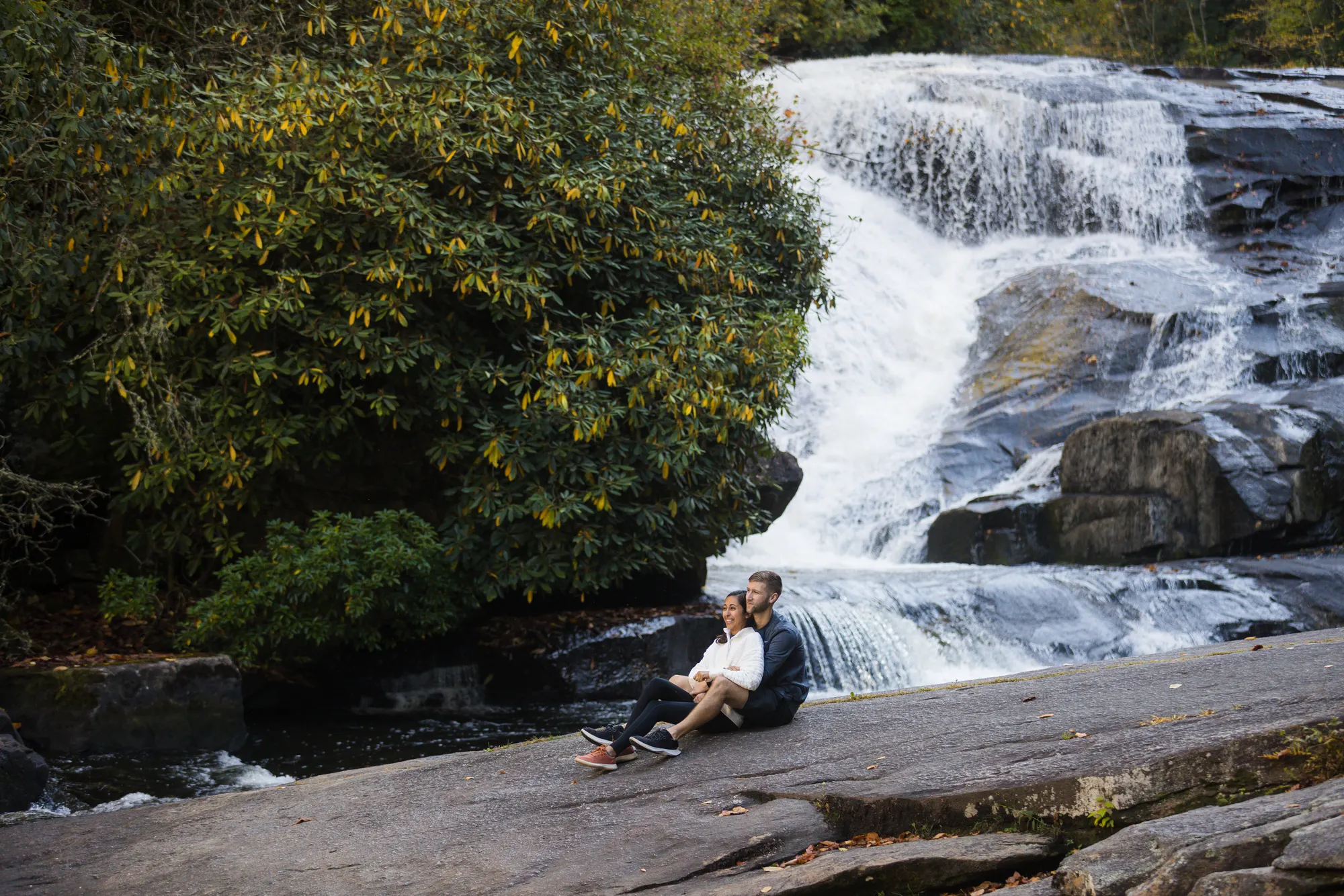 Couple at the lower cascade of Triple Falls with fall color, the waterfall where Katniss found Peeta in The Hunger Games