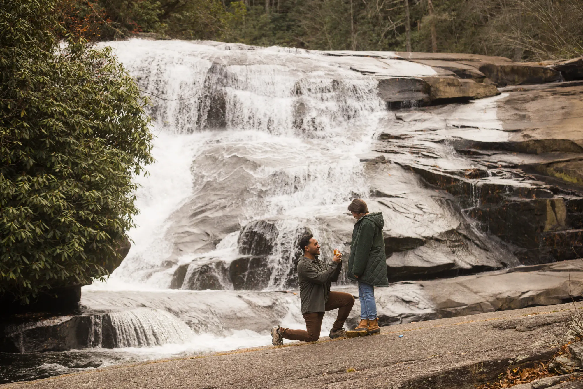 Man proposing at Triple Falls in DuPont State Forest with autumn leaves on the rock