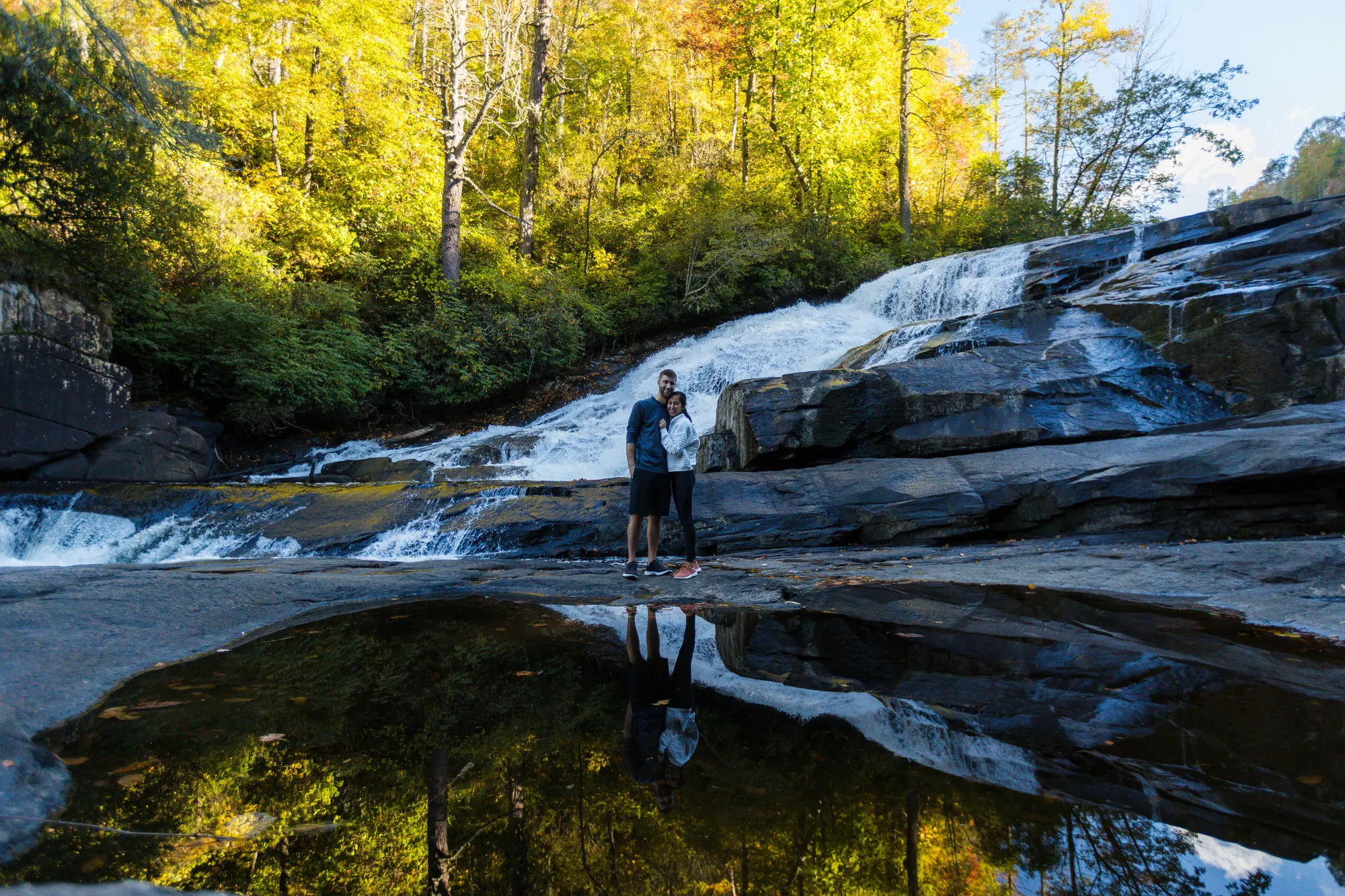 Engaged couple reflected in a still pool below a waterfall at DuPont State Forest, golden light