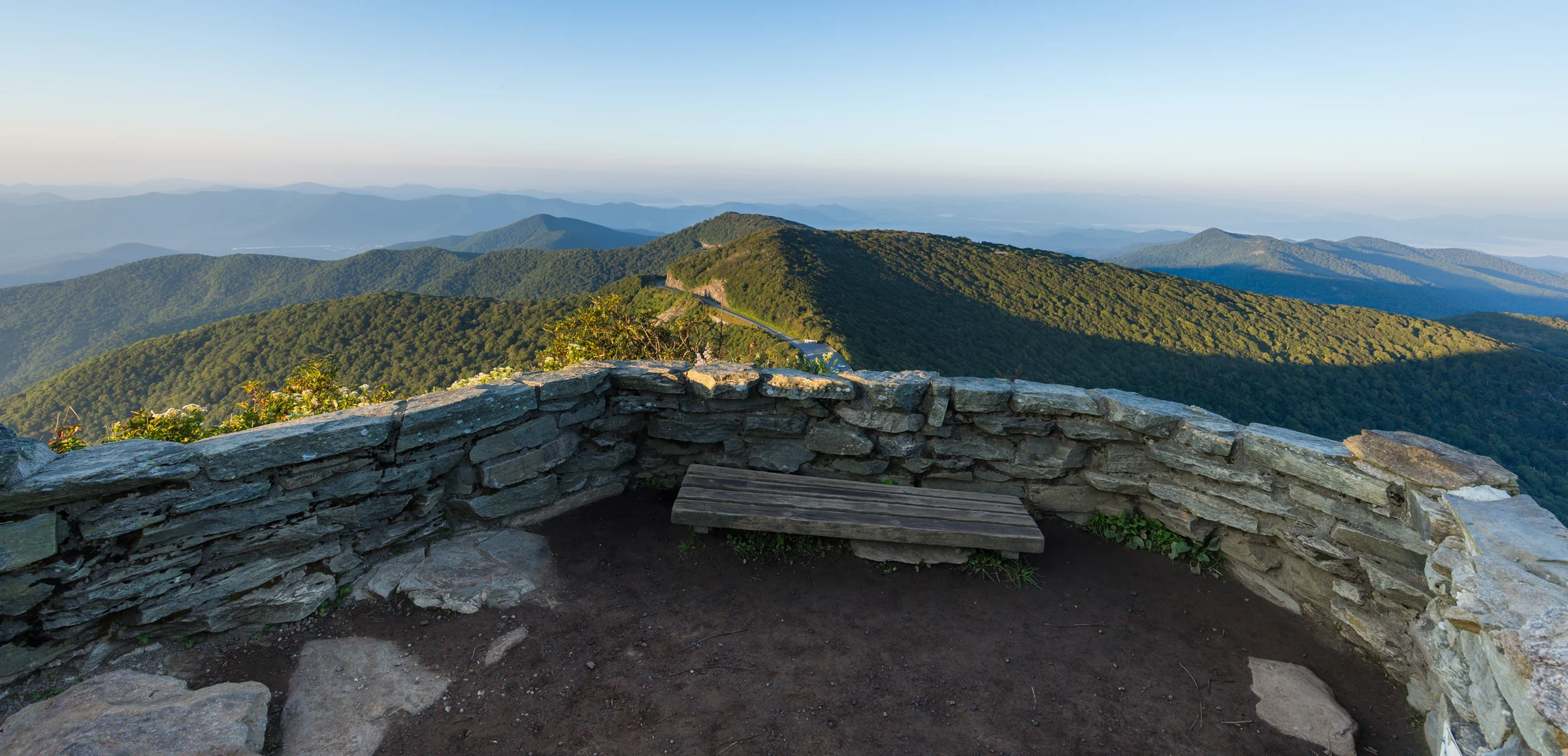 A stone bench built into the summit wall on Craggy Pinnacle, worn smooth, with the heath bald behind it
