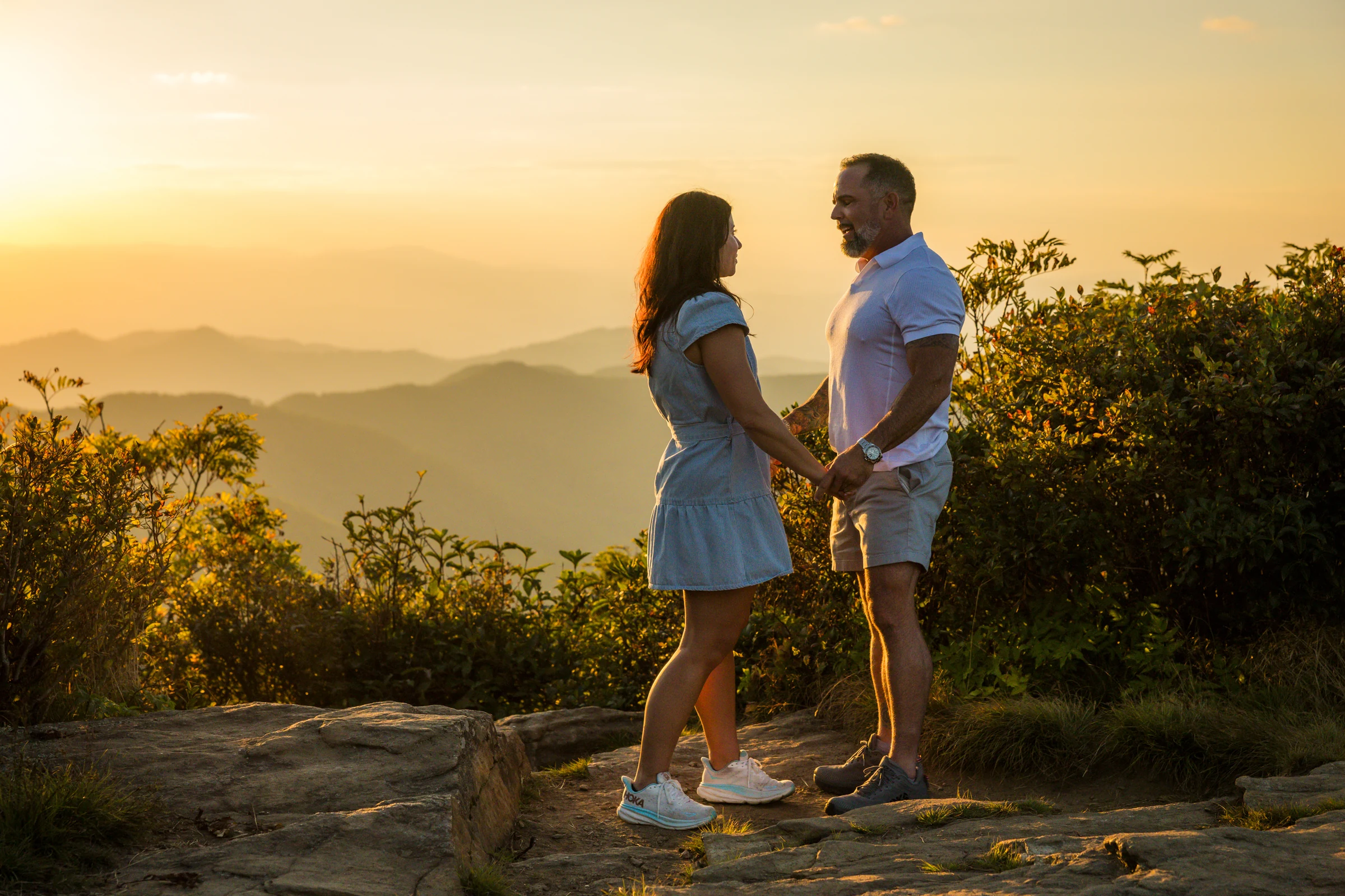 Scott and Jaci holding hands at golden hour on the west ledge of Craggy Pinnacle, Blue Ridge Mountains behind them