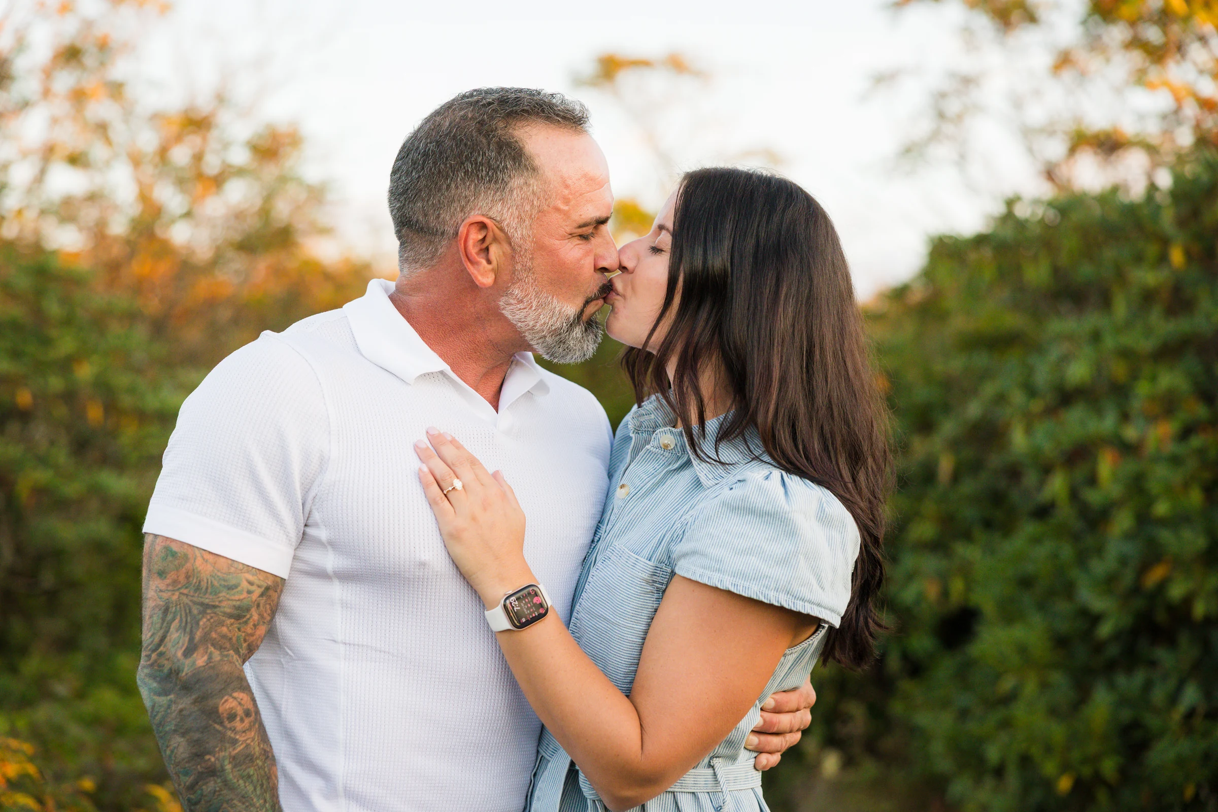 Scott kisses Jaci as she holds up her engagement ring on the west ledge of Craggy Pinnacle, warm sunset light and mountain ridges behind them