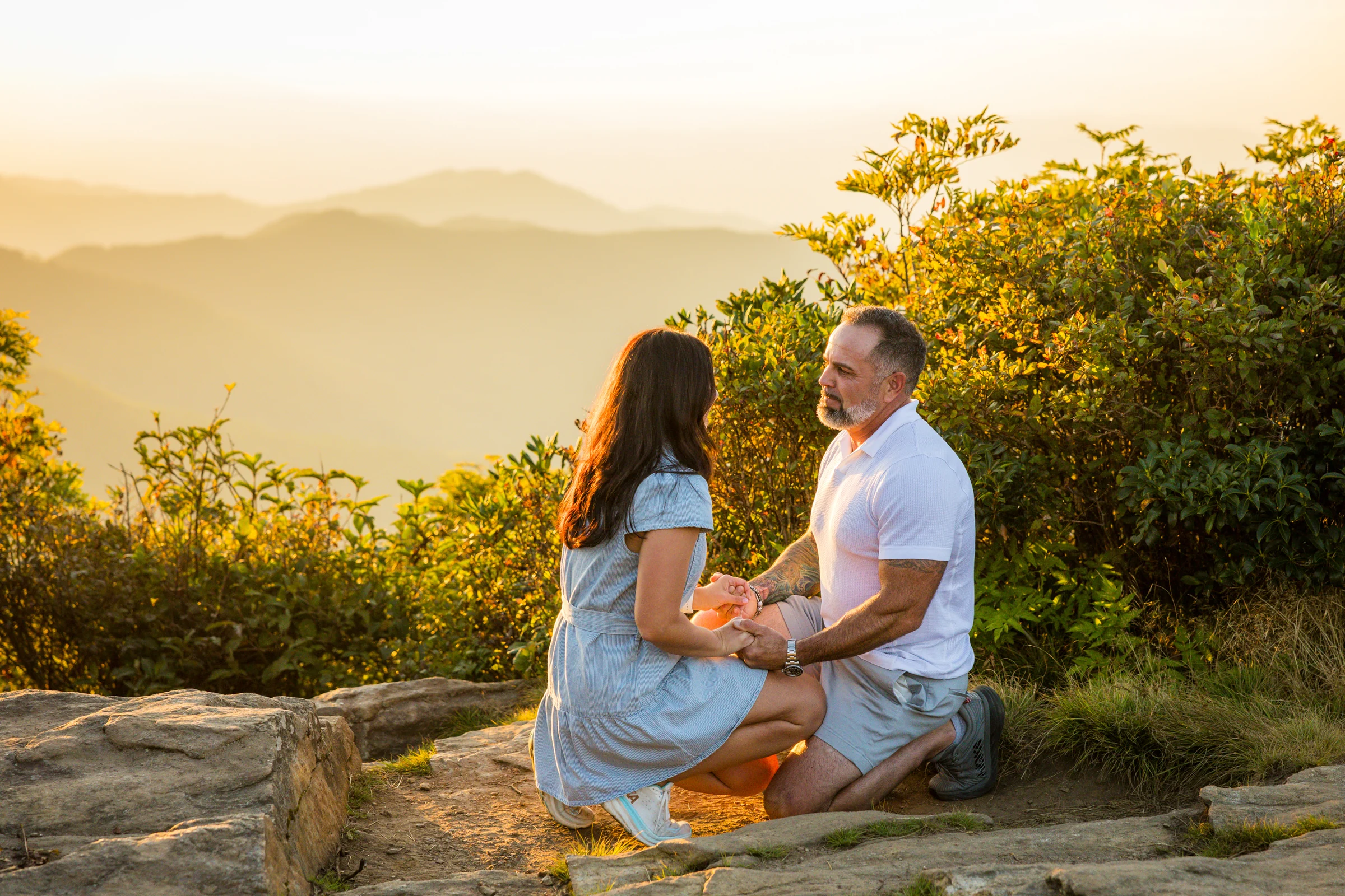 Close view of Scott and Jaci's hands during the proposal on Craggy Pinnacle as the ring box opens, warm sunset light on the rock ledge