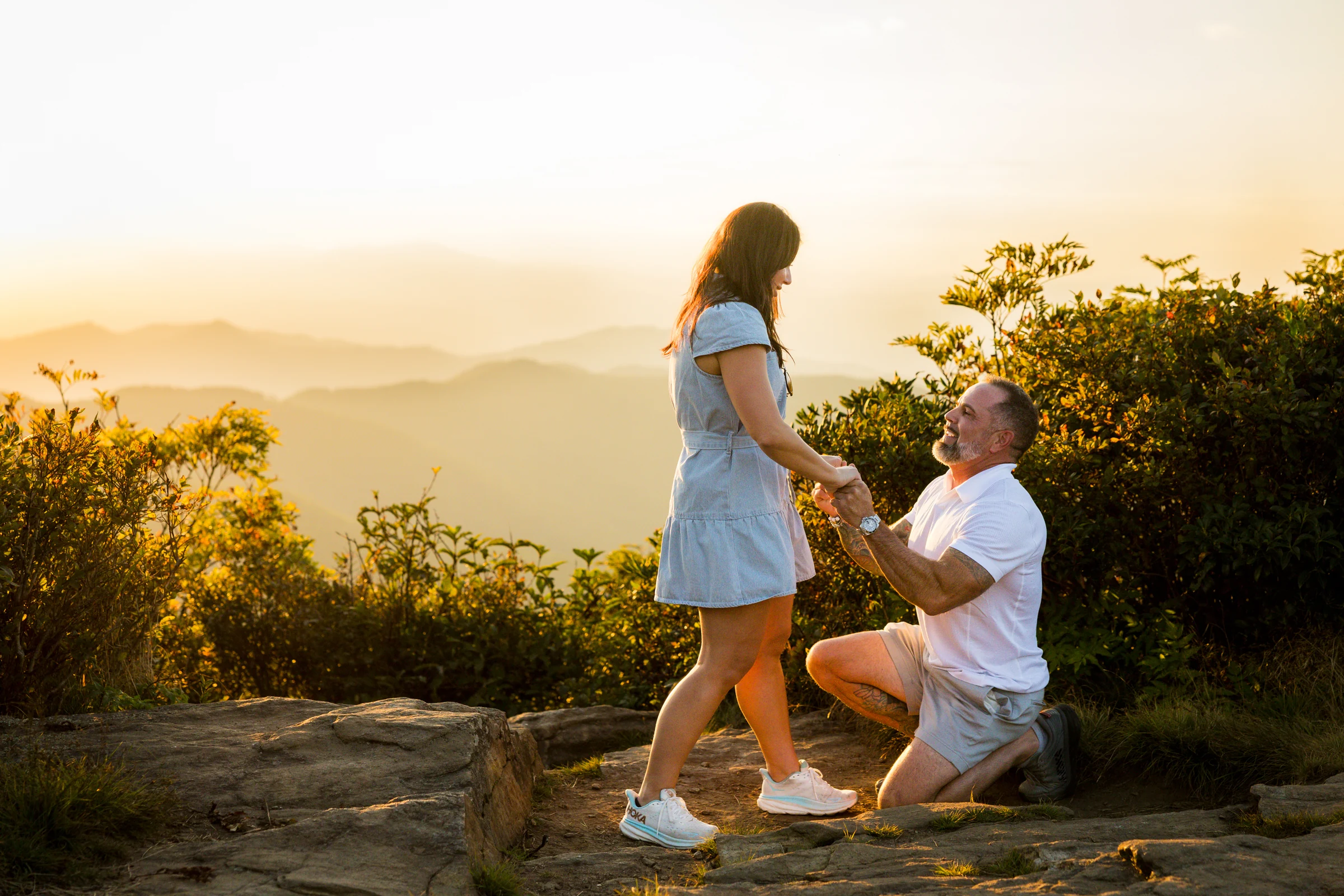Scott and Jaci standing together on the west ledge of Craggy Pinnacle after the proposal, layered Blue Ridge Mountains in the distance