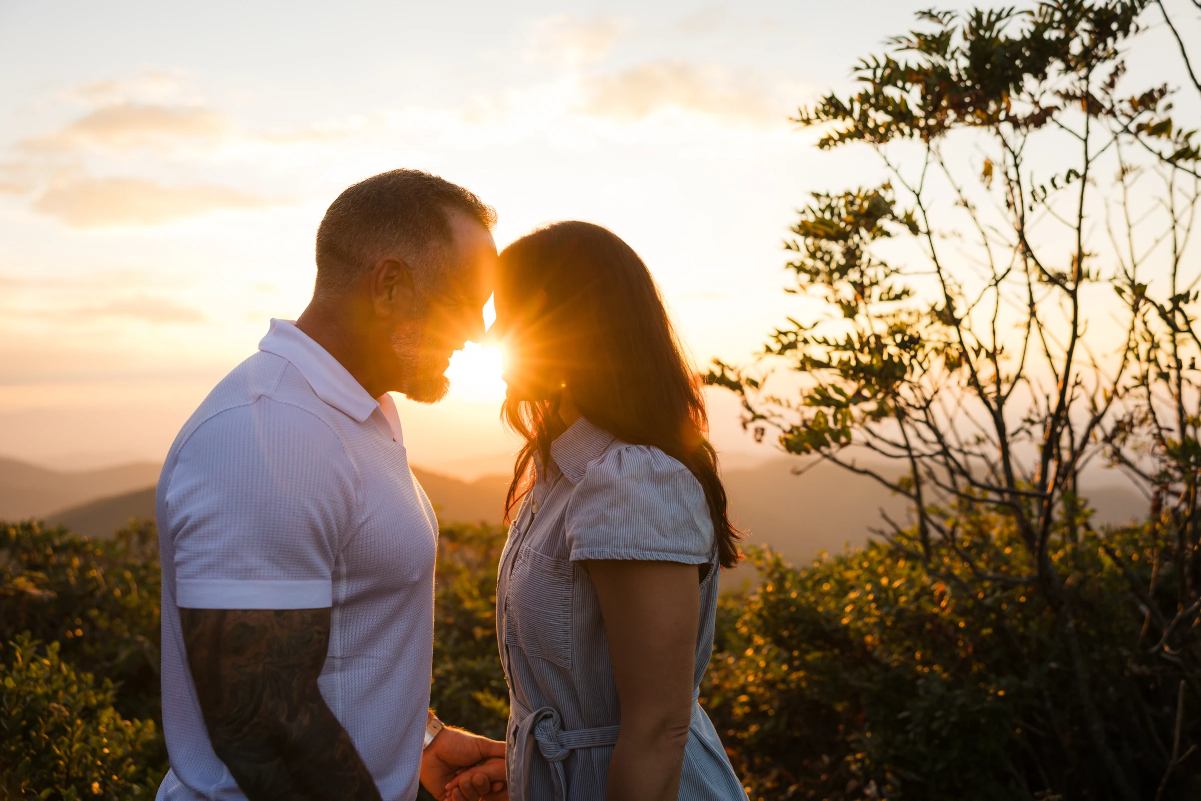 A sunburst flares between Scott and Jaci's faces as they lean together at sunset on Craggy Pinnacle