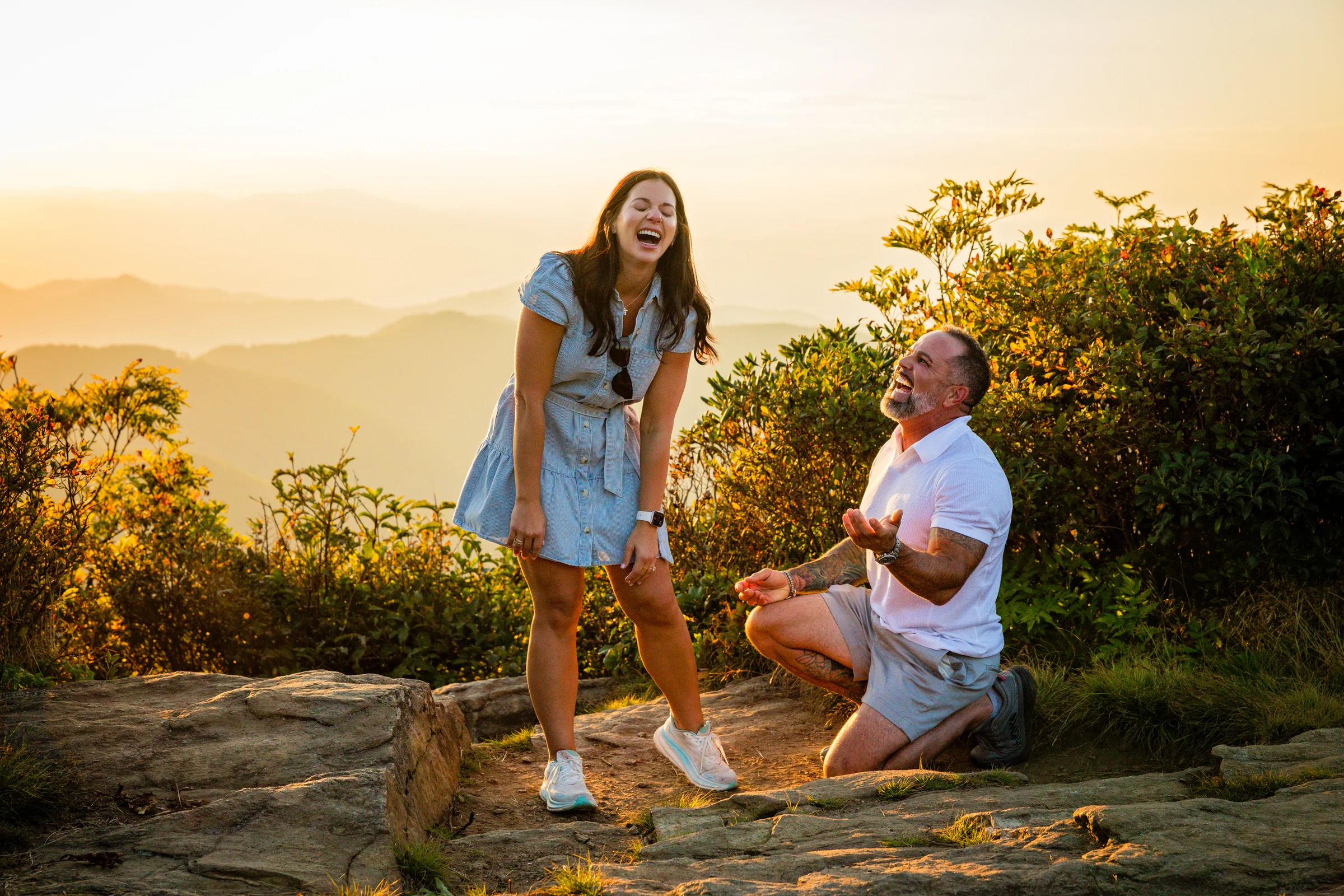Jaci's surprised reaction as Scott proposes on Craggy Pinnacle, the Blue Ridge Mountains and sunset sky behind her