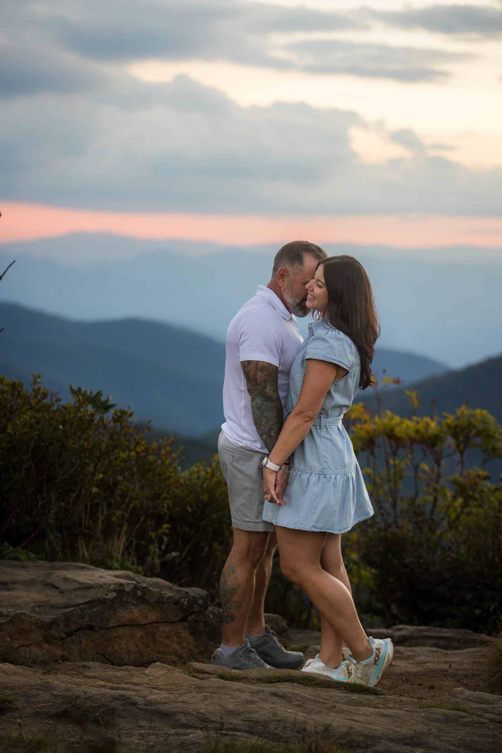 Vertical portrait of Scott and Jaci on the west ledge of Craggy Pinnacle with the Blue Ridge Mountains fading behind them at sunset